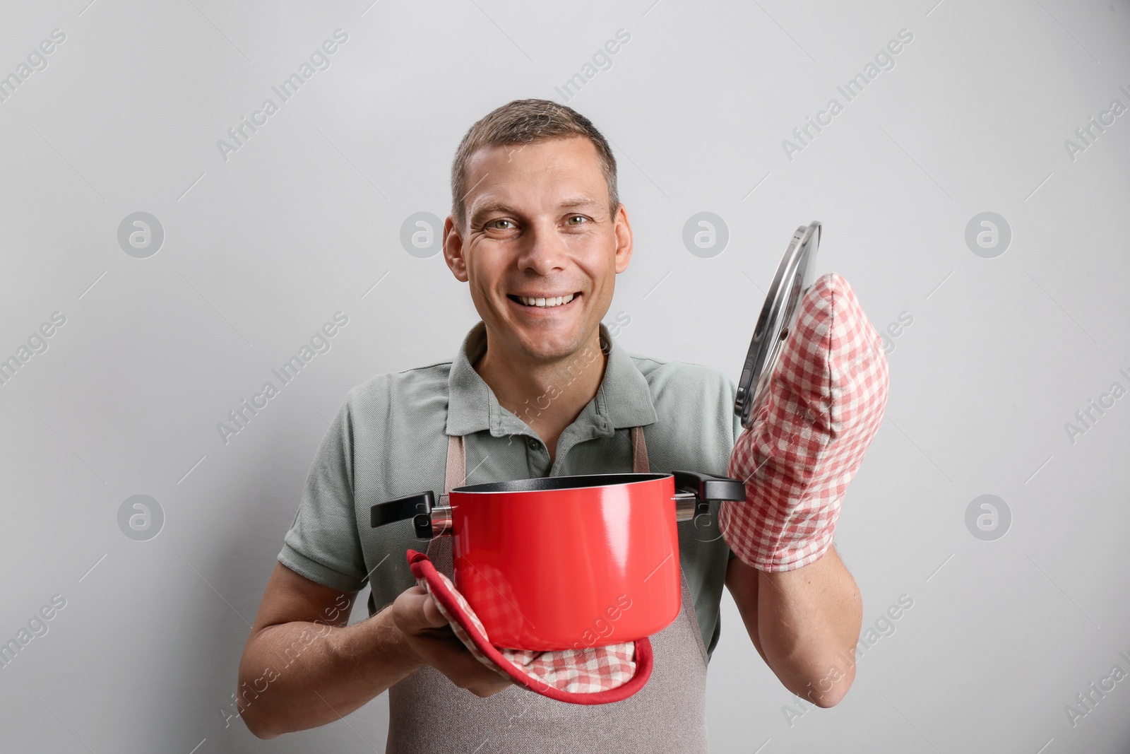 Photo of Happy man with cooking pot on light grey background