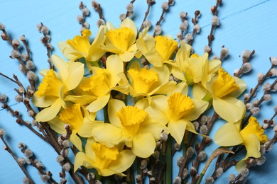 Bouquet of beautiful yellow daffodils and willow flowers on light blue wooden table, top view