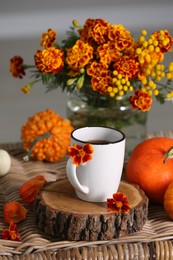 Beautiful autumn composition with cup of drink and flowers on wicker table