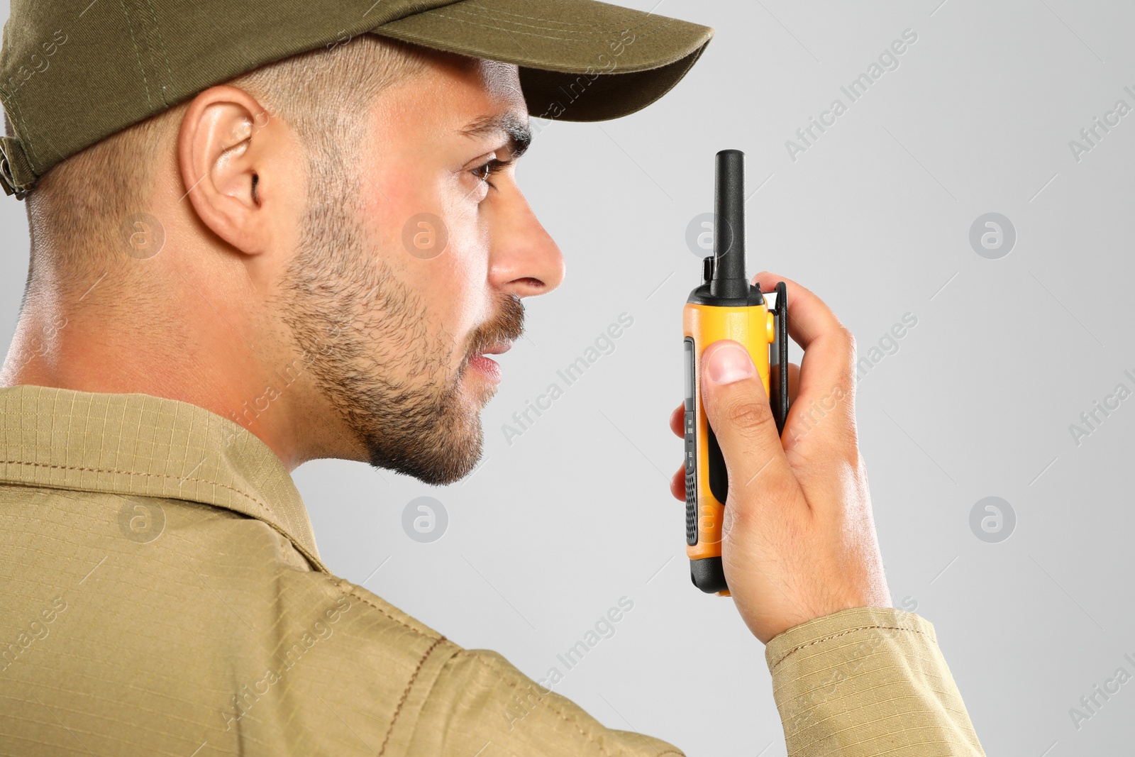 Photo of Male security guard in uniform using portable radio transmitter on grey background, closeup