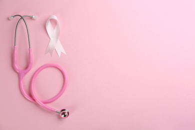 Photo of Pink ribbon as breast cancer awareness symbol and stethoscope on color background, flat lay. Space for text