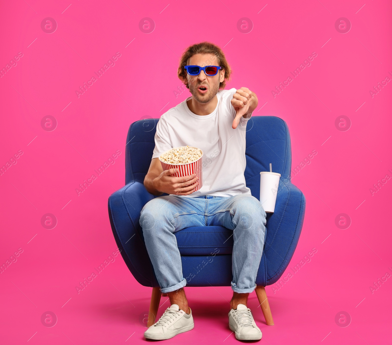 Photo of Emotional man with 3D glasses, popcorn and beverage sitting in armchair during cinema show on color background