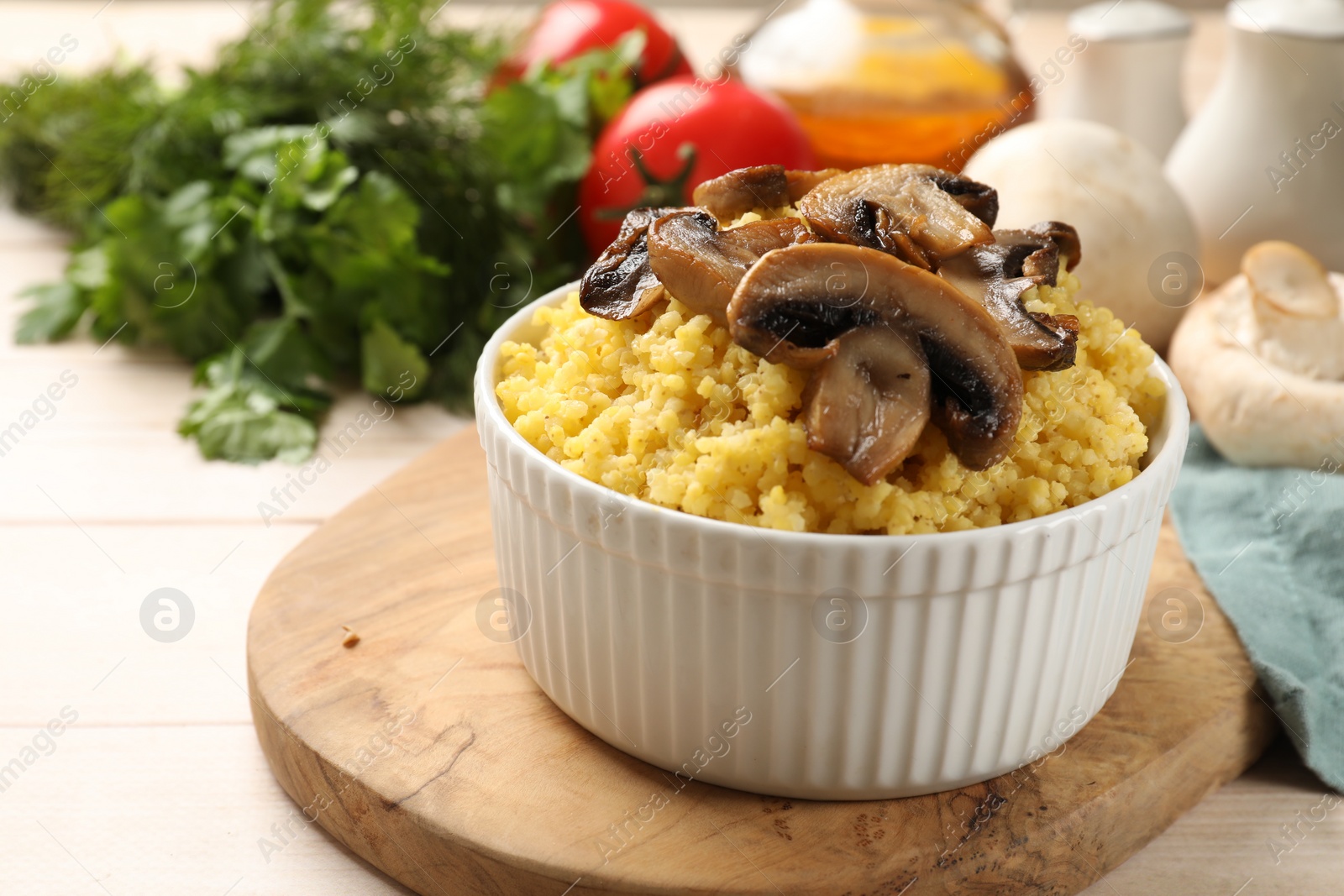 Photo of Tasty millet porridge and mushrooms in bowl on light wooden table, closeup. Space for text