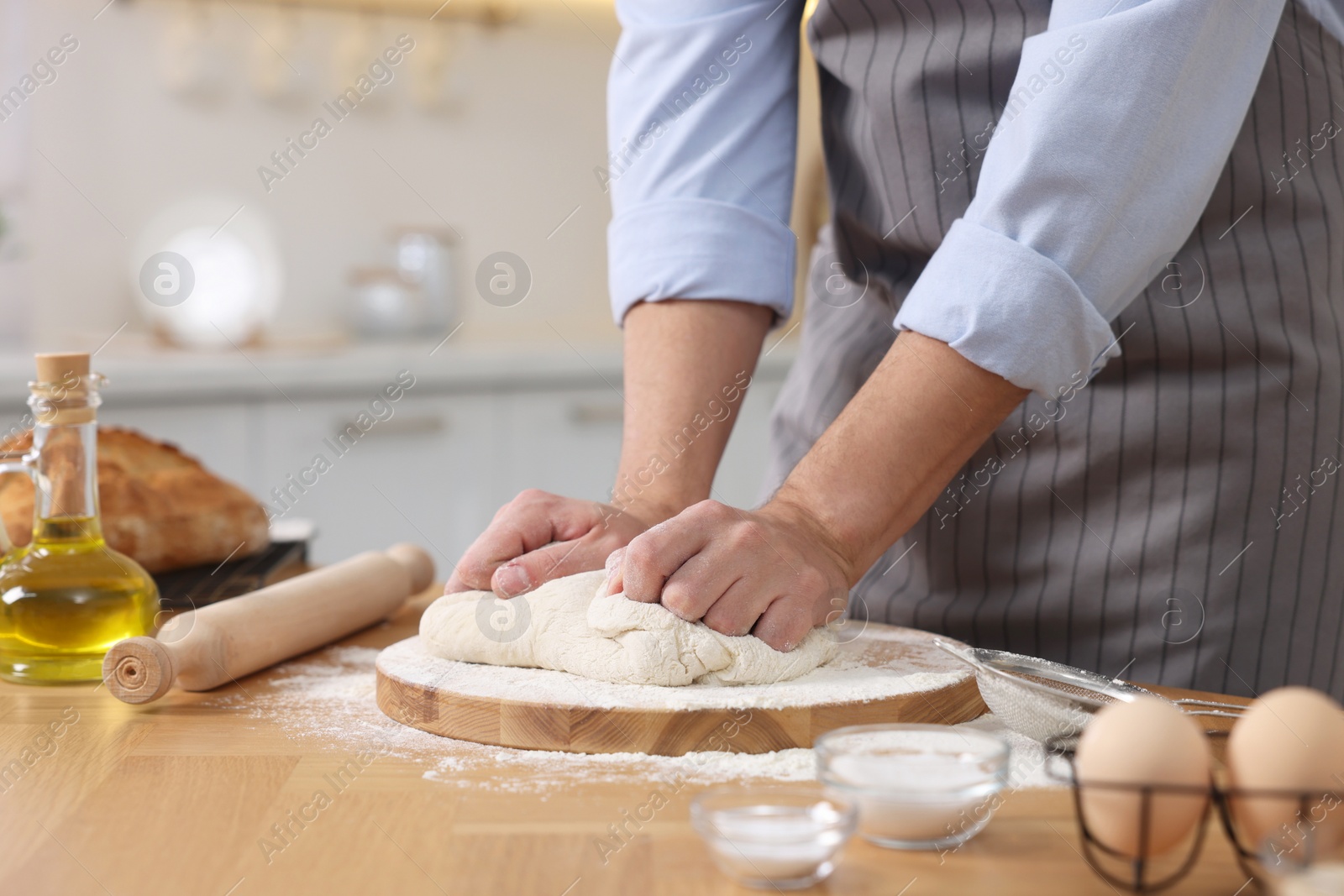 Photo of Making bread. Man kneading dough at wooden table in kitchen, closeup