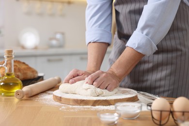 Making bread. Man kneading dough at wooden table in kitchen, closeup