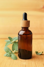 Bottle of mint essential oil and fresh herb on wooden table