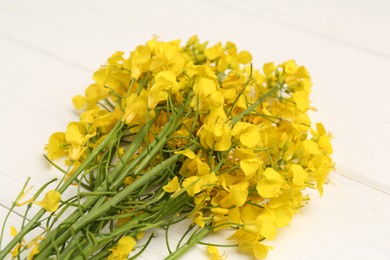 Photo of Beautiful rapeseed flowers on white wooden table, closeup