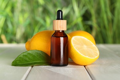 Photo of Bottle of essential oil with lemons and leaf on white wooden table against blurred background, closeup