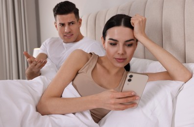 Photo of Internet addiction. Woman with smartphone ignoring her boyfriend in bedroom