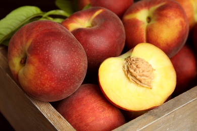 Photo of Tasty peaches and leaves in wooden crate, closeup