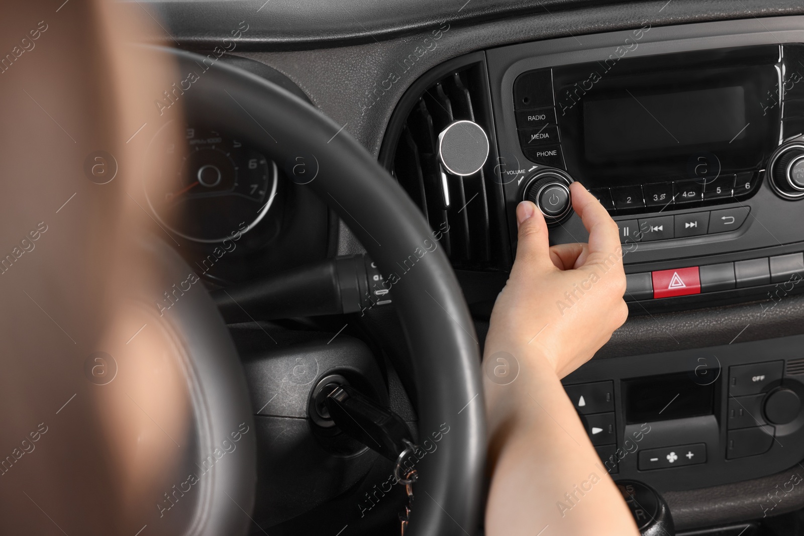 Photo of Listening to radio while driving. Woman turning volume button on vehicle audio in car, closeup