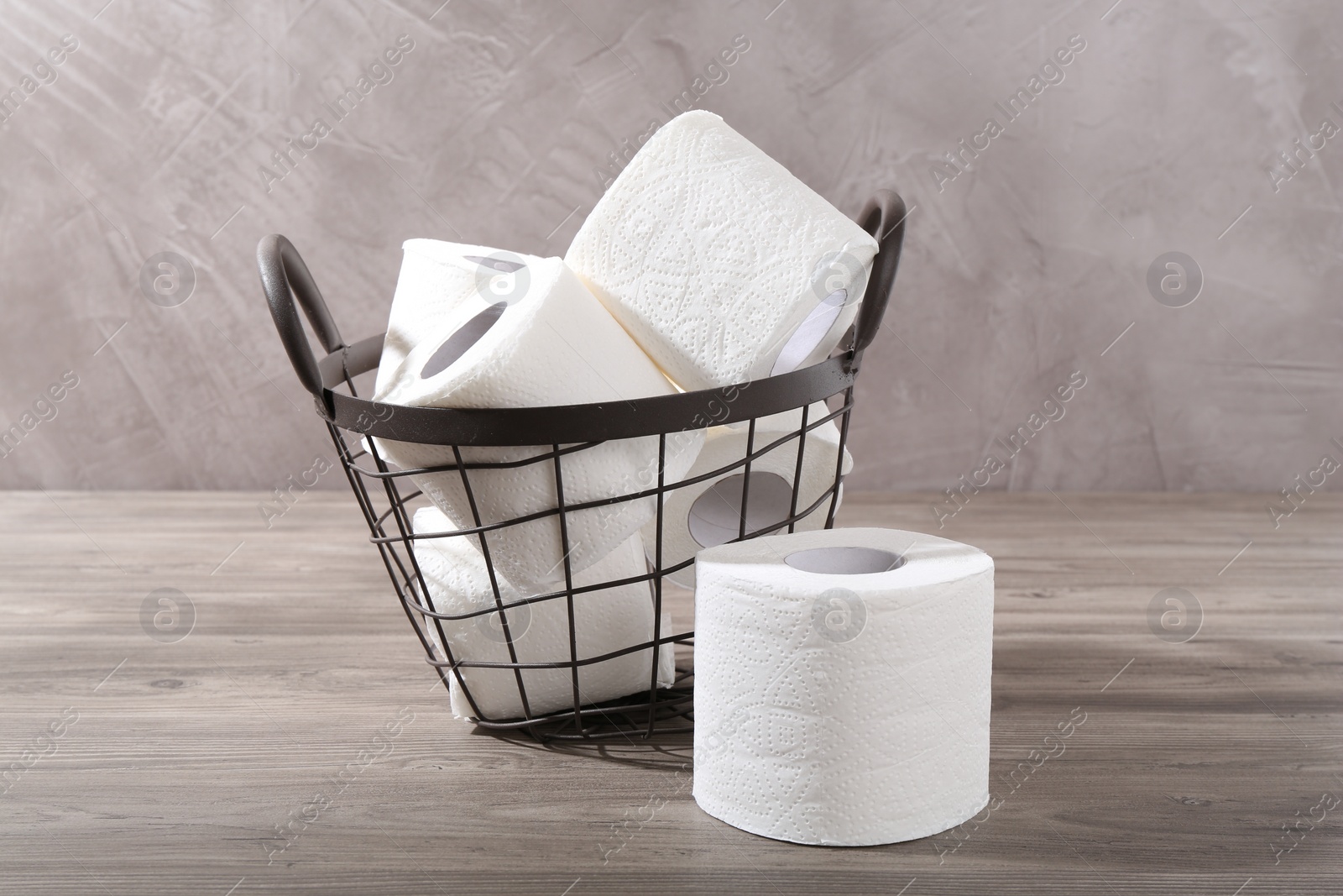 Photo of Soft toilet paper rolls in metal basket on wooden table, closeup