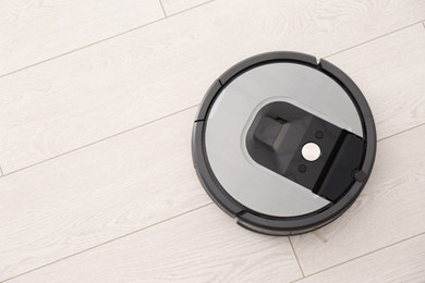 Photo of Modern robotic vacuum cleaner on wooden floor, top view. Space for text