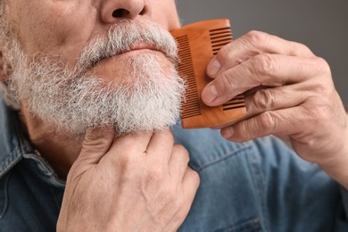 Photo of Man combing beard on grey background, closeup