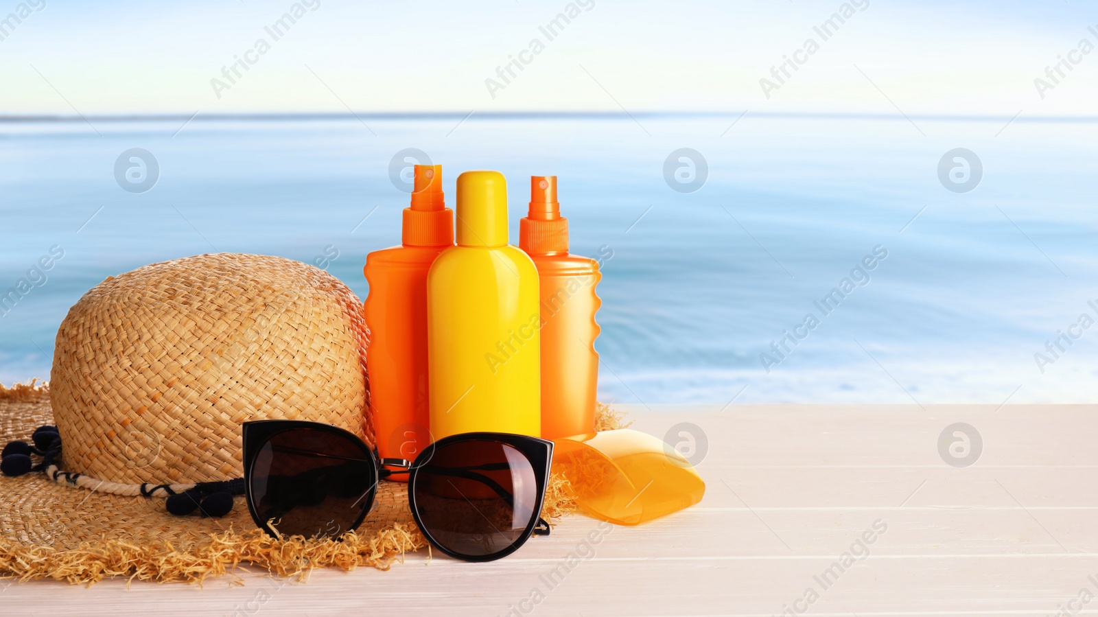 Image of Set of sun protection products and stylish accessories on wooden table near sea. Space for text