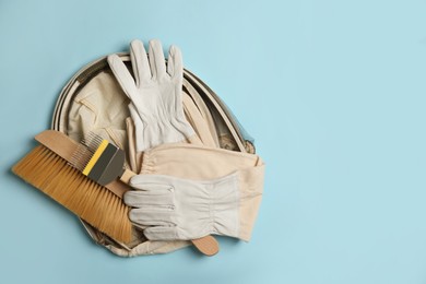 Photo of Beekeeping tools and uniform on light blue background, top view. Space for text