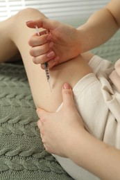 Photo of Diabetes. Woman making insulin injection into her leg on bed indoors, closeup