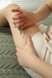 Diabetes. Woman making insulin injection into her leg on bed indoors, closeup