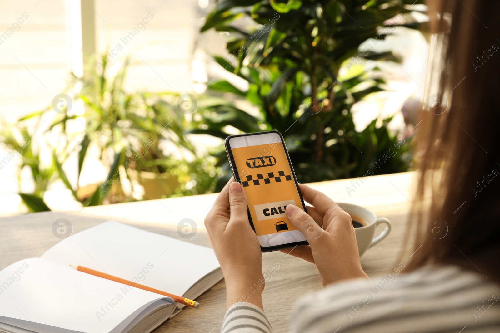 Photo of Woman ordering taxi with smartphone at wooden table, closeup