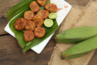 Delicious fried bananas, fresh fruits and cut limes on wooden table, flat lay