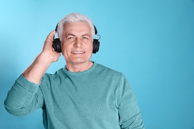 Photo of Mature man enjoying music in headphones on color background. Space for text