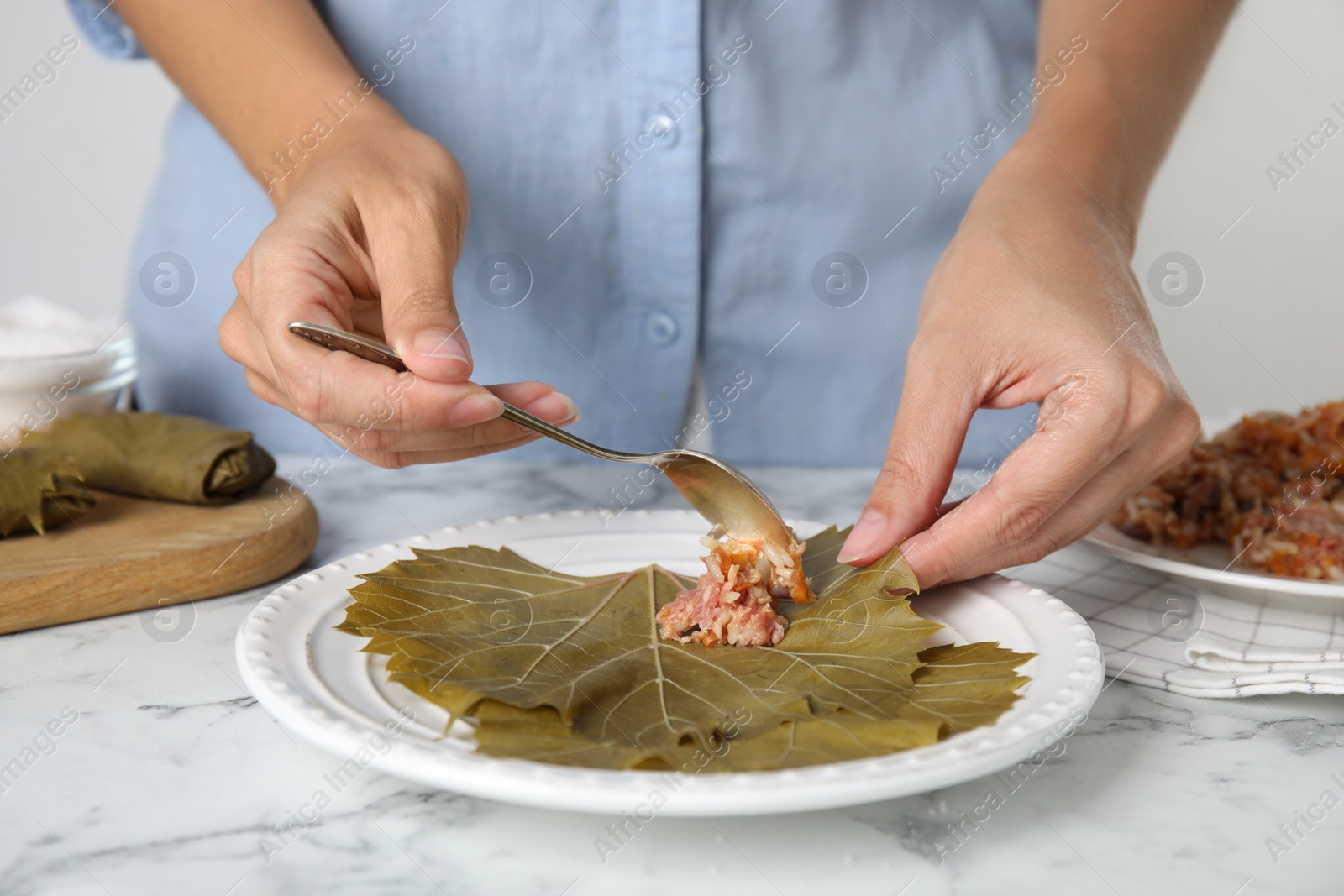 Photo of Woman preparing stuffed grape leaves at white marble table, closeup