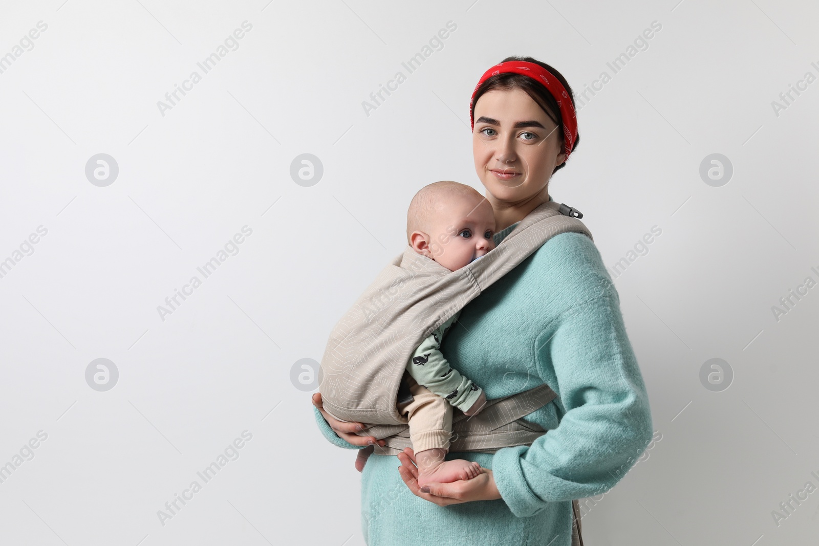 Photo of Mother holding her child in sling (baby carrier) on light grey background. Space for text