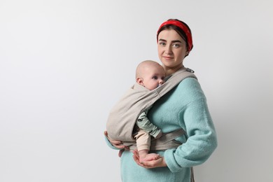 Mother holding her child in sling (baby carrier) on light grey background. Space for text