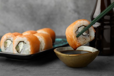 Photo of Dipping tasty sushi roll with salmon into soy sauce on grey table