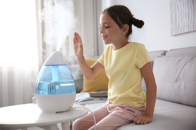 Photo of Little girl near modern air humidifier at home