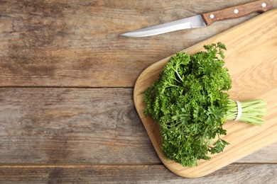 Photo of Cutting board with fresh green parsley and knife on wooden table, flat lay. Space for text