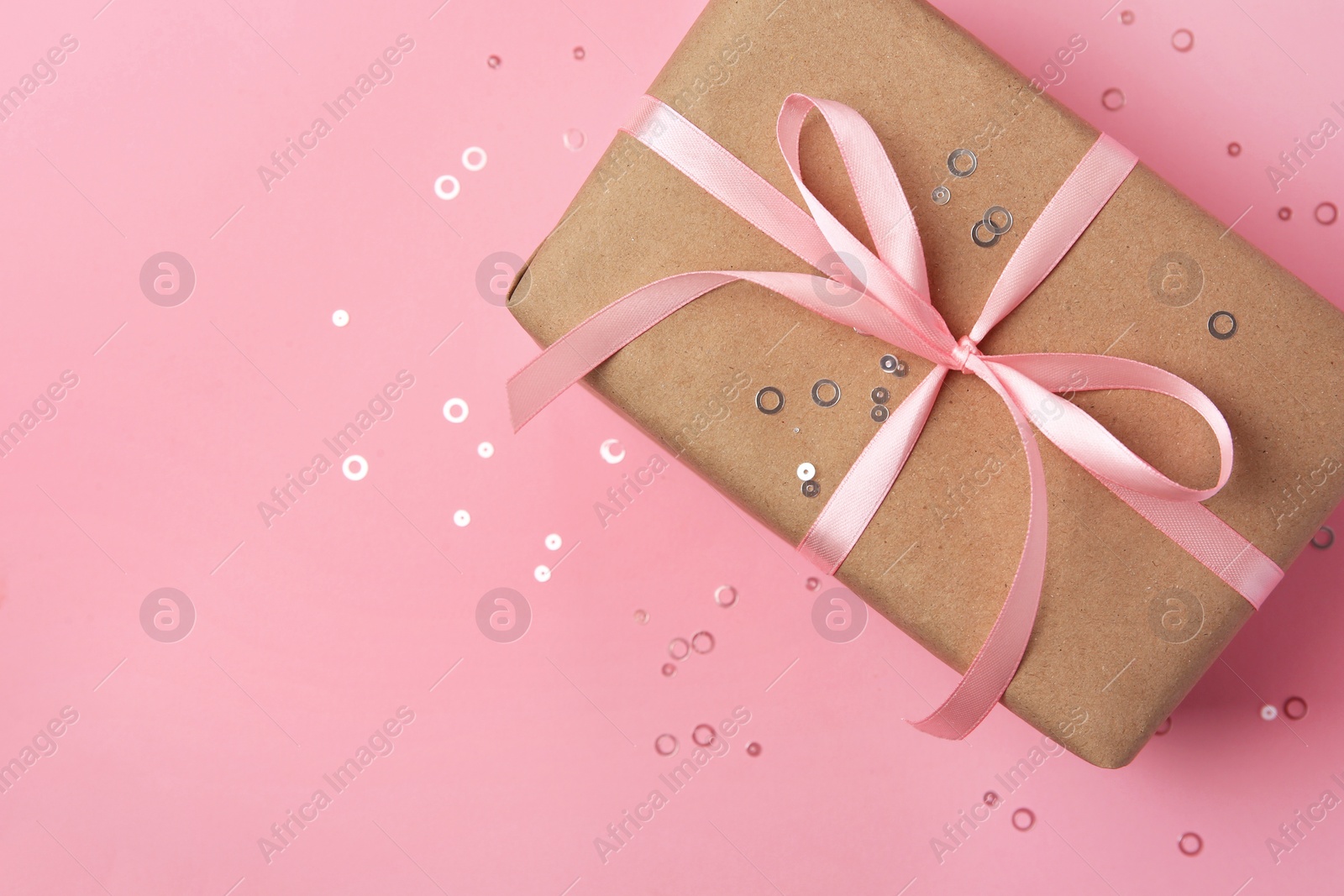Photo of Beautiful gift box with bow and confetti on pink background, top view. Space for text