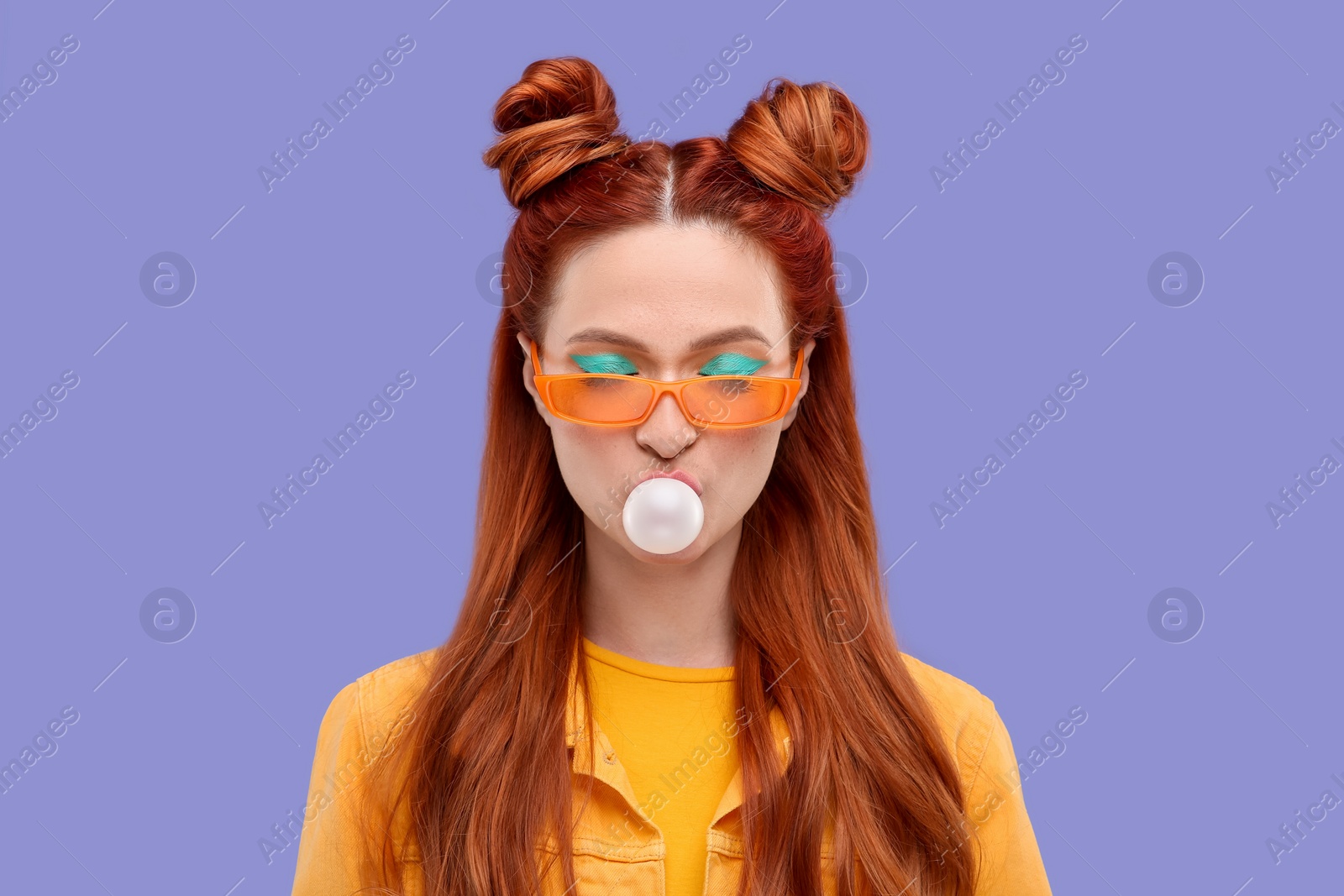 Photo of Beautiful woman with bright makeup and closed eyes blowing bubble gum on violet background