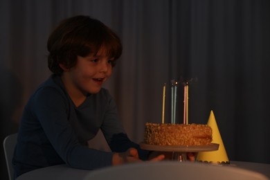 Cute boy with birthday cake at table indoors