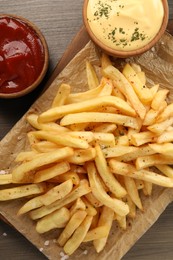 Delicious french fries served with sauces on wooden table, flat lay