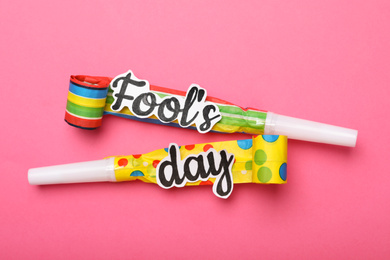 Photo of Party horns with words FOOL'S DAY on pink background, flat lay. April holiday