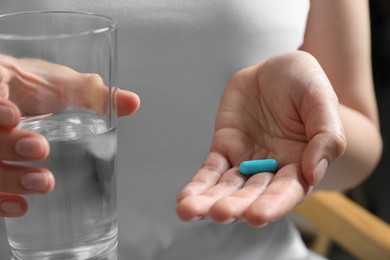 Woman holding glass of water and pill, closeup