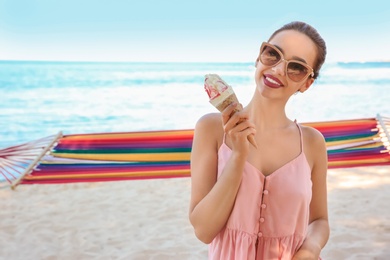 Photo of Young woman eating ice cream near hammock at seaside