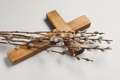 Photo of Wooden cross and willow branches on light grey background. Easter attributes