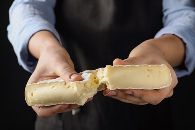 Photo of Woman breaking delicious brie cheese on black background, closeup