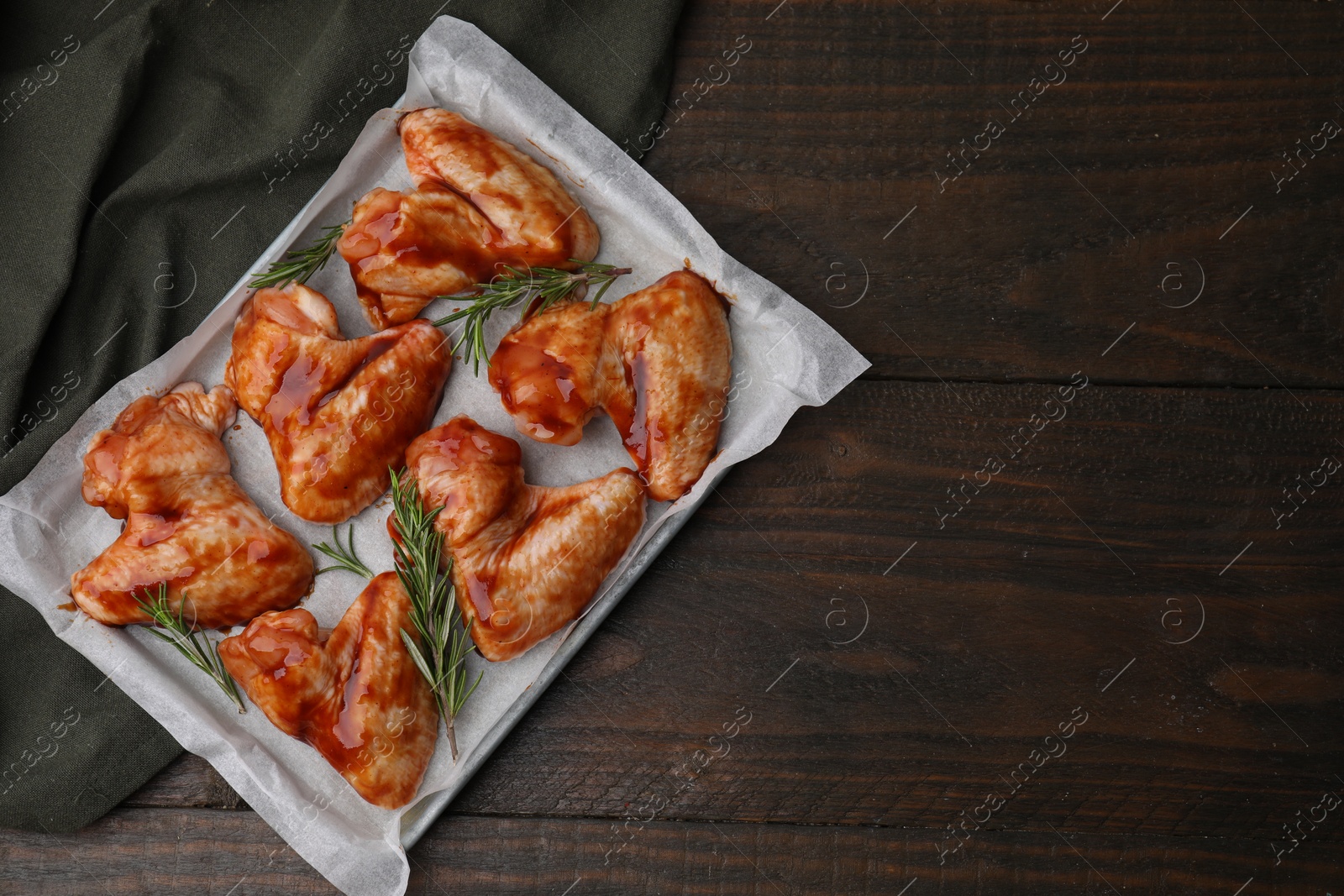 Photo of Raw marinated chicken wings and rosemary on wooden table, top view. Space for text