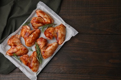 Photo of Raw marinated chicken wings and rosemary on wooden table, top view. Space for text