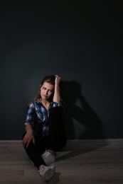 Photo of Depressed young woman sitting on floor in darkness