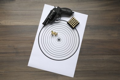 Photo of Shooting target, handgun and bullets on wooden table, top view