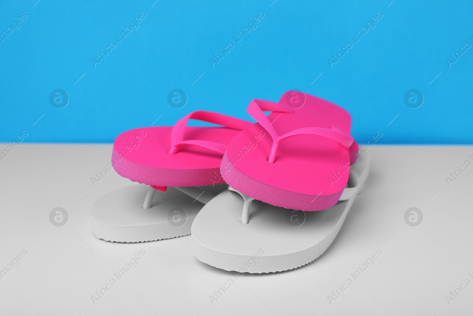 Photo of Different flip flops on white table against light blue background