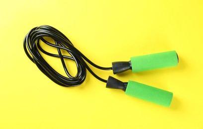 Photo of Skipping rope on yellow background, top view. Sports equipment