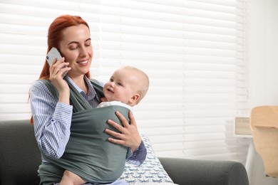 Photo of Mother talking on smartphone while holding her child in sling (baby carrier) indoors