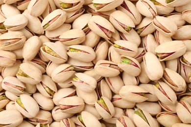 Photo of Tasty unpeeled pistachios as background, top view