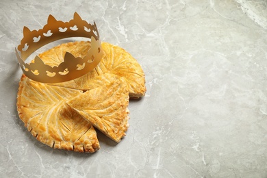 Photo of Traditional galette des Rois with paper crown on grey marble table, above view. Space for text