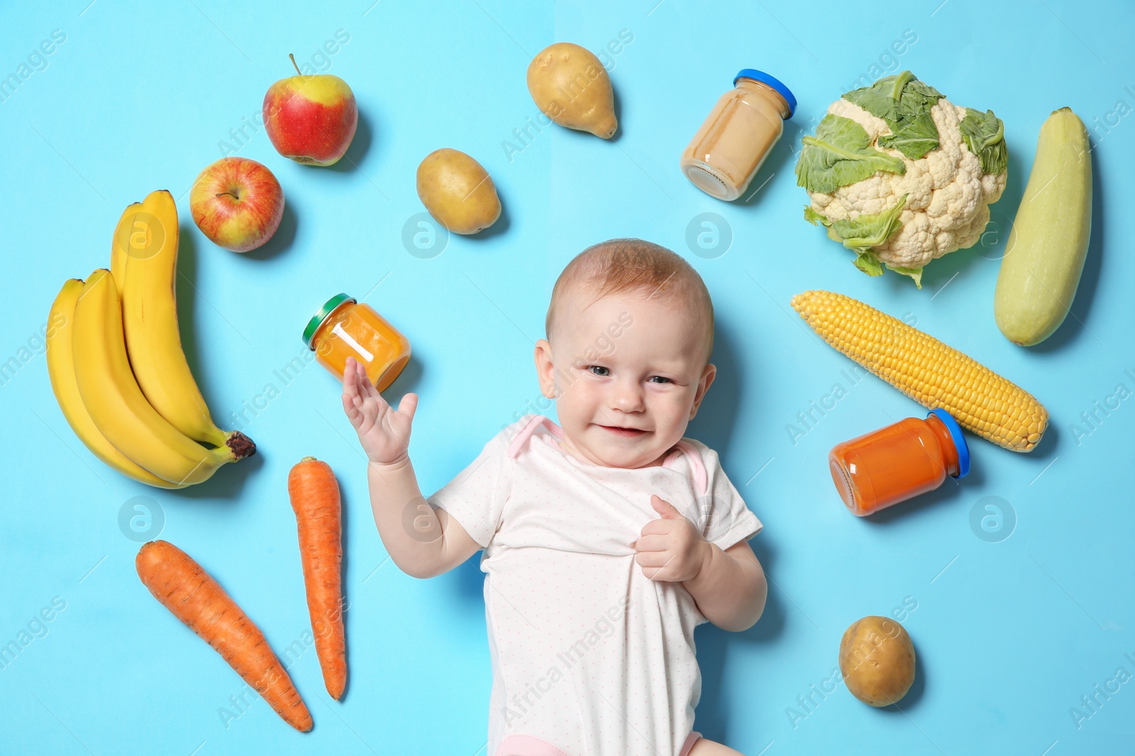 Photo of Cute little child with ingredients and purees in jars on color background, top view. Baby food